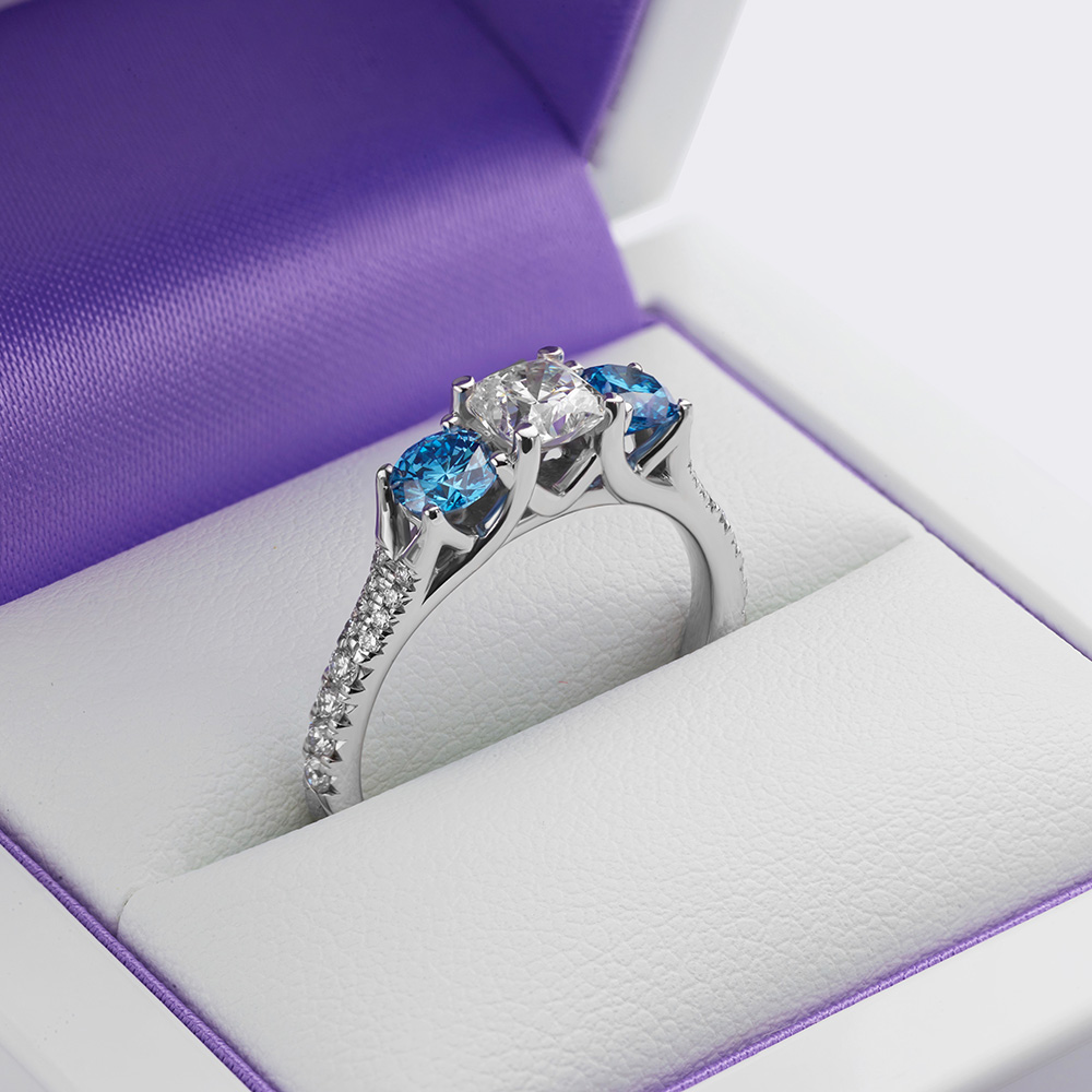 Blue diamond engagement ring created to hold our clients original Hearts on Fire diamond with intense lab-grown blue diamonds on either side. 